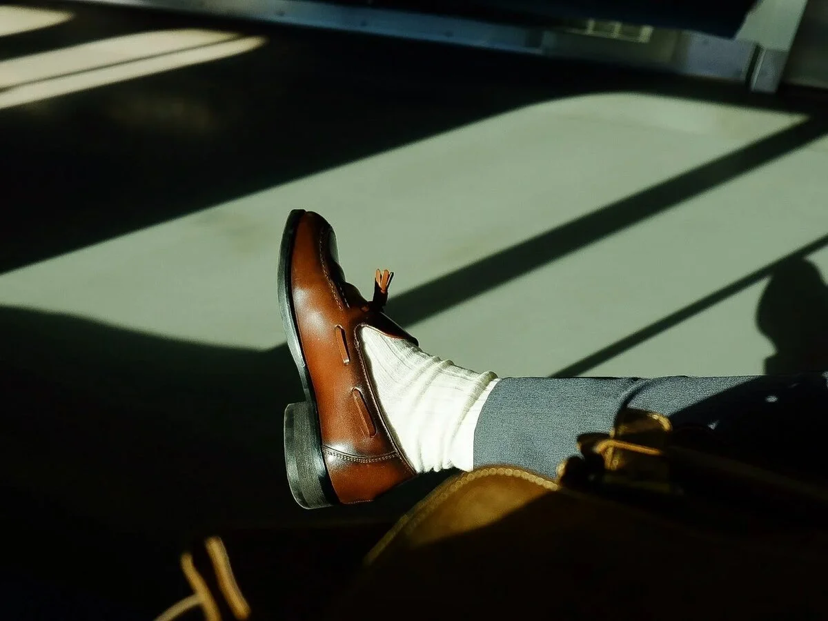 A man dressed in a suit and tie is seated on a train, sporting men's high sole shoes.